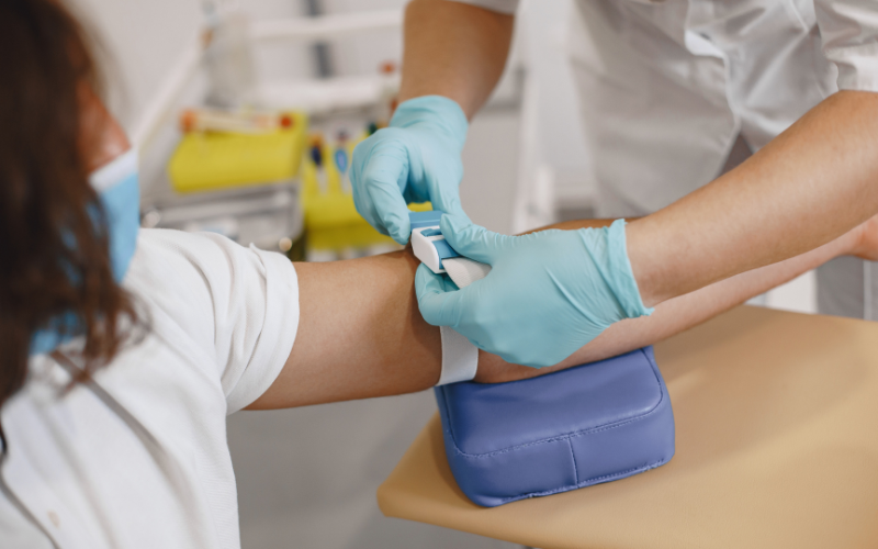 Healthcare professional wearing gloves placing a tourniquet on a patient's arm before drawing blood.