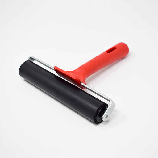 A black rubber roller with a red plastic handle rests on a white surface.