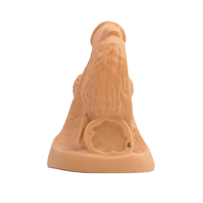 A light brown, sculpted figurine of a seated figure, possibly a dog or similar creature, rests on a plain white background. The figurine has a circular design near its base.