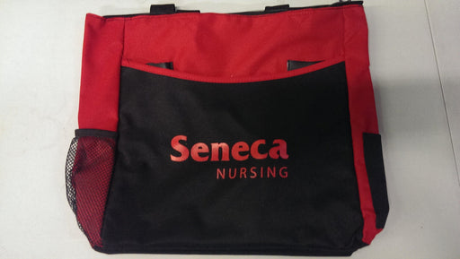 A red and black tote bag sits upright. The bag displays the logo "Seneca Nursing" in a stylized font. Side mesh pockets are visible.